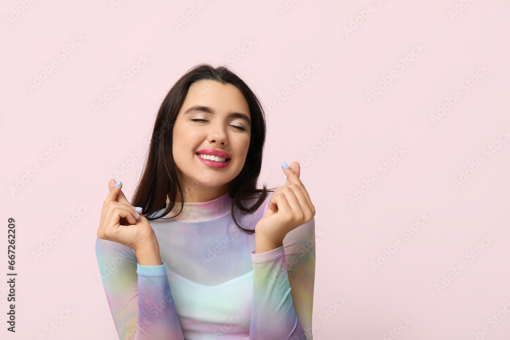 Beautiful young happy woman showing hearts gesture on pink background