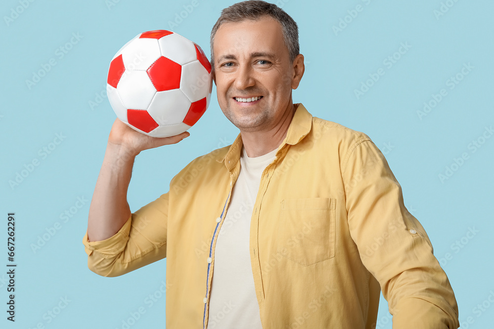 Handsome mature man with soccer ball on blue background