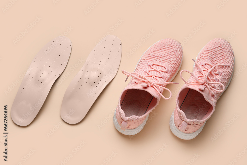 Pair of stylish pink sneakers with orthopedic insoles on beige background