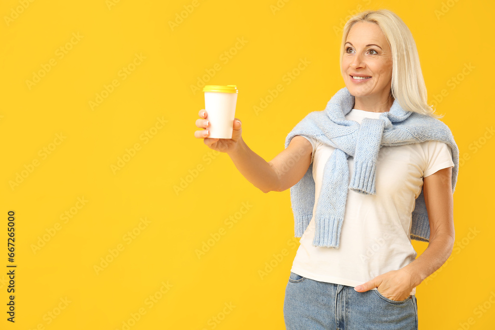 Mature woman with cup of coffee and warm scarf on yellow background