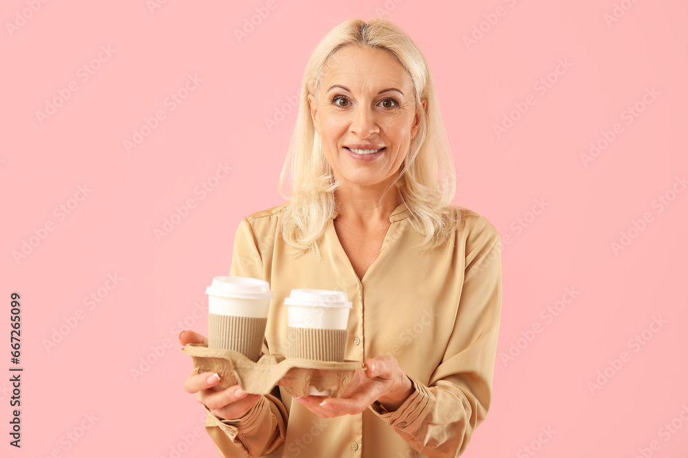 Mature woman with cups of coffee on pink background