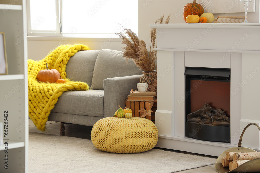 Autumn interior of light living room with grey sofa, fireplace and pumpkins