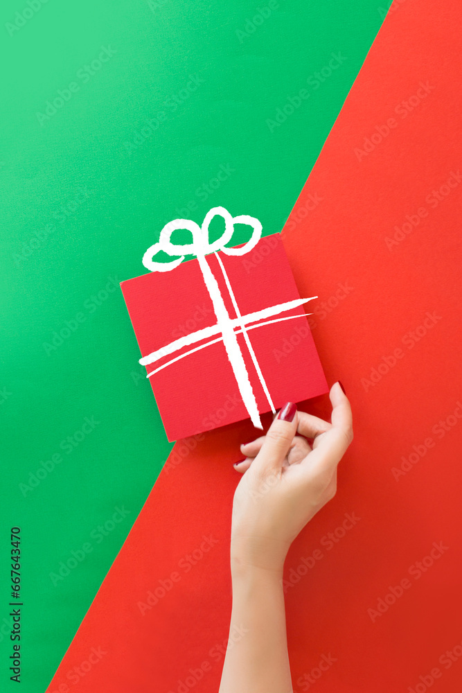 Hand holding a gift boxe on green and red background.