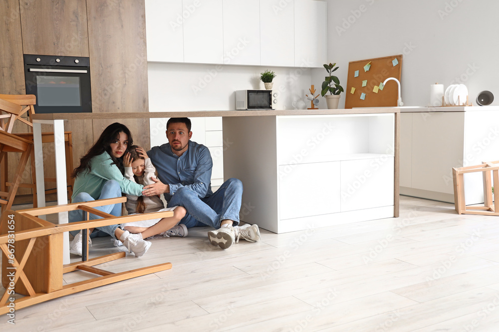 Scared family hiding under dining table during earthquake in kitchen