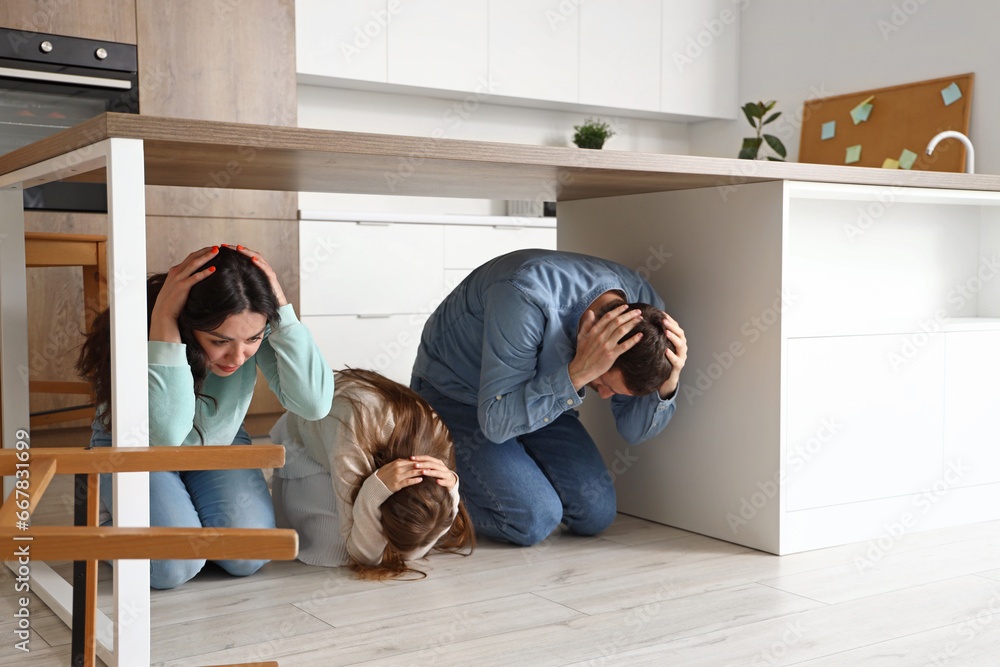 Scared family hiding under dining table during earthquake in kitchen