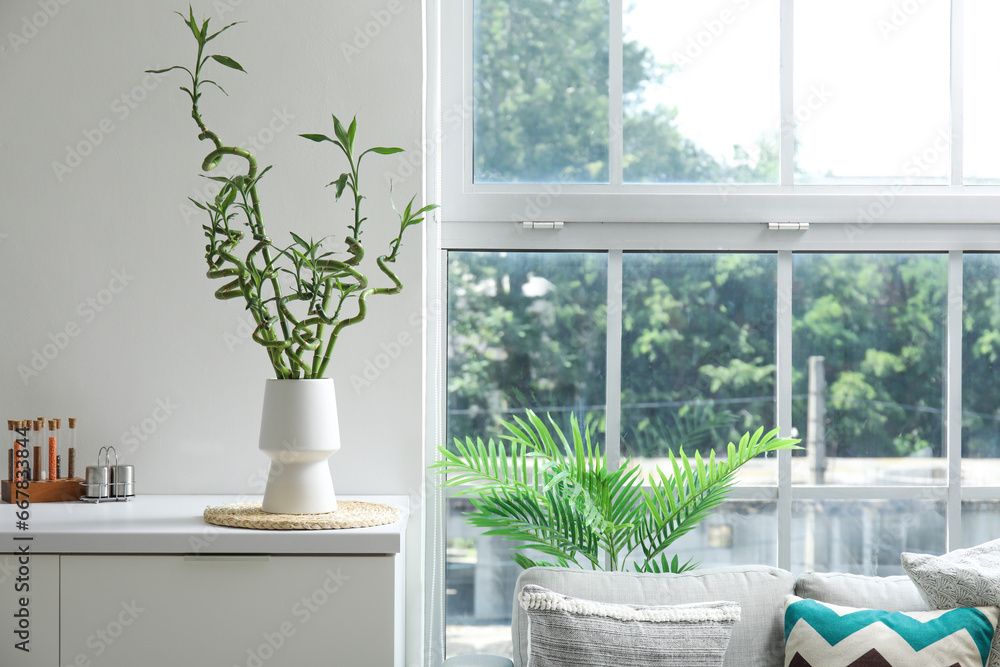 Vase with green bamboo stems on table near window