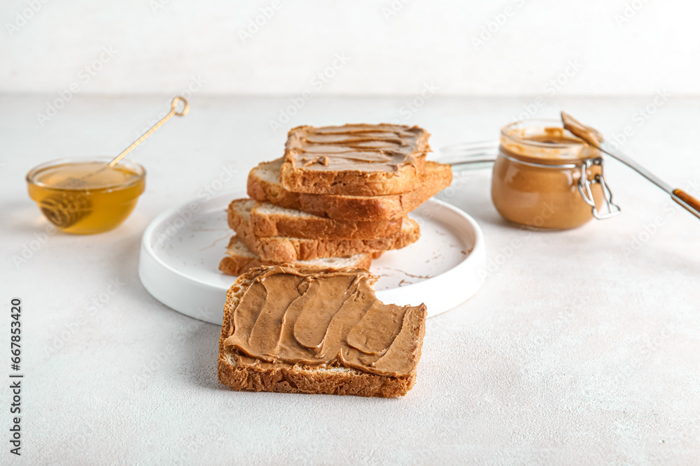 Plate of toasts with peanut butter and bowl of honey on white background