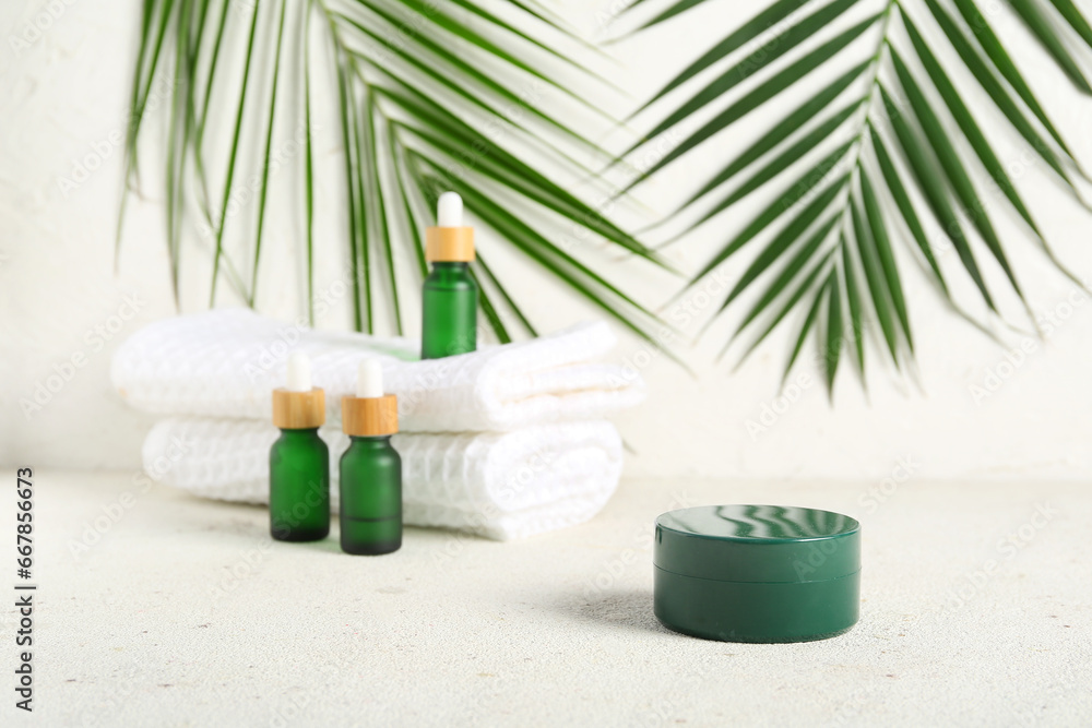 Set of cosmetic products, clean towels and palm leaves on light background