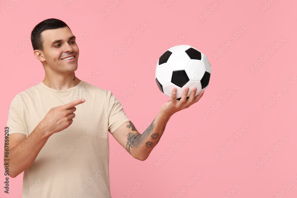 Handsome young man pointing at soccer ball on pink background