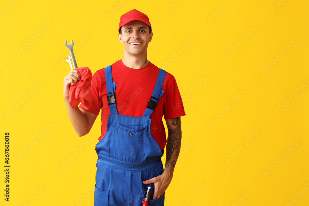 Male car mechanic with rag and wrenches on yellow background