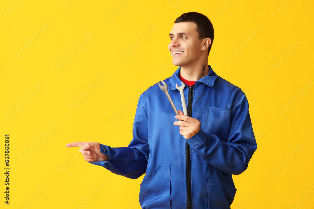 Male car mechanic with wrenches pointing at something on yellow background