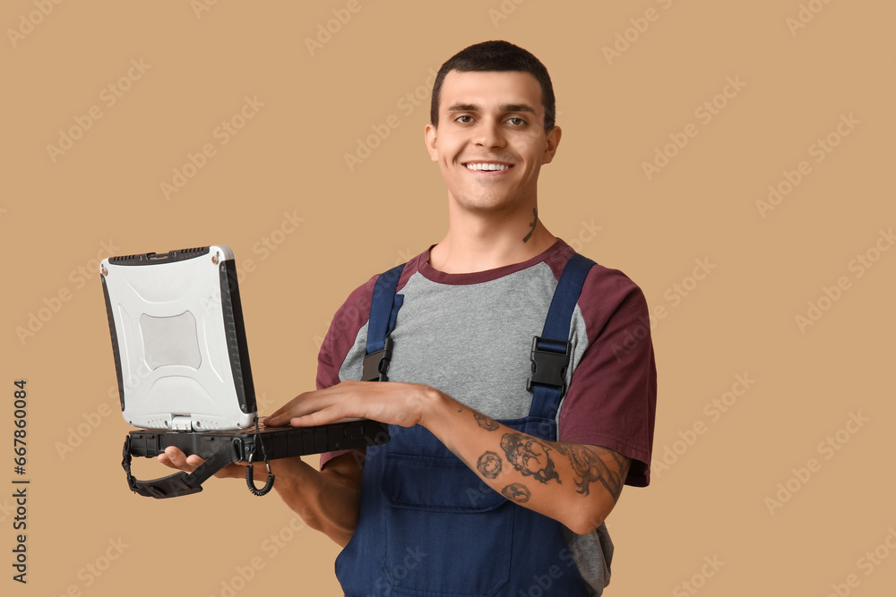 Male car mechanic with laptop on beige background