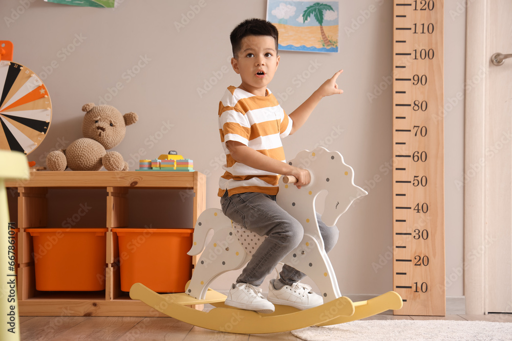 Little Asian boy rocking on horse at home