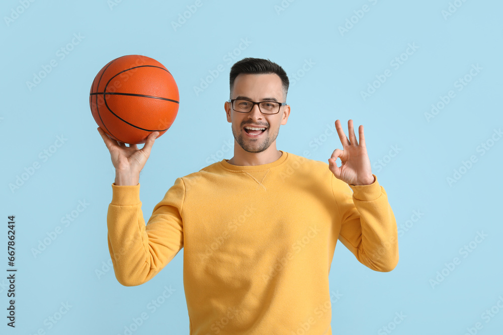 Happy young man with ball showing OK on blue background