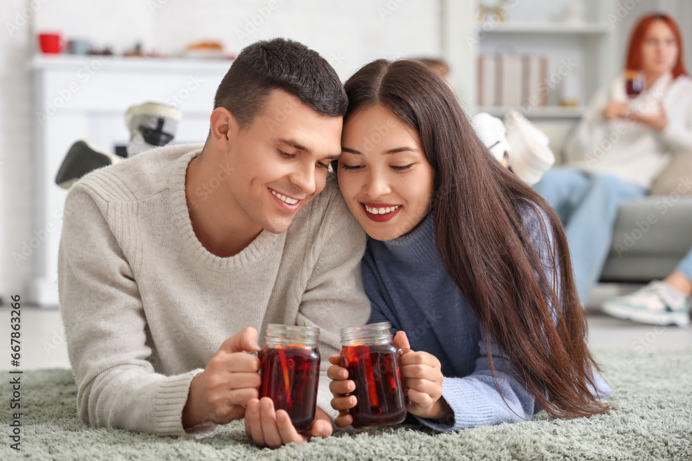 Happy couple with glasses of warm mulled wine lying on floor in living room at party