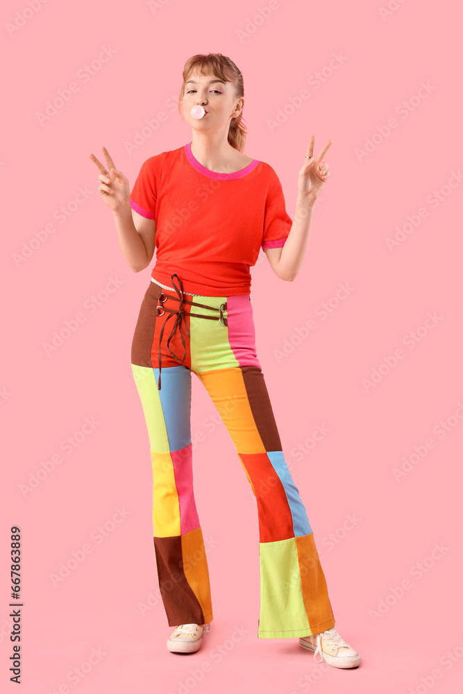 Beautiful young woman with chewing gum showing victory gesture on pink background