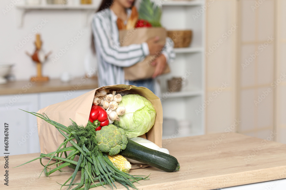 Young Asian woman with shopping bags full of fresh food at table in kitchen