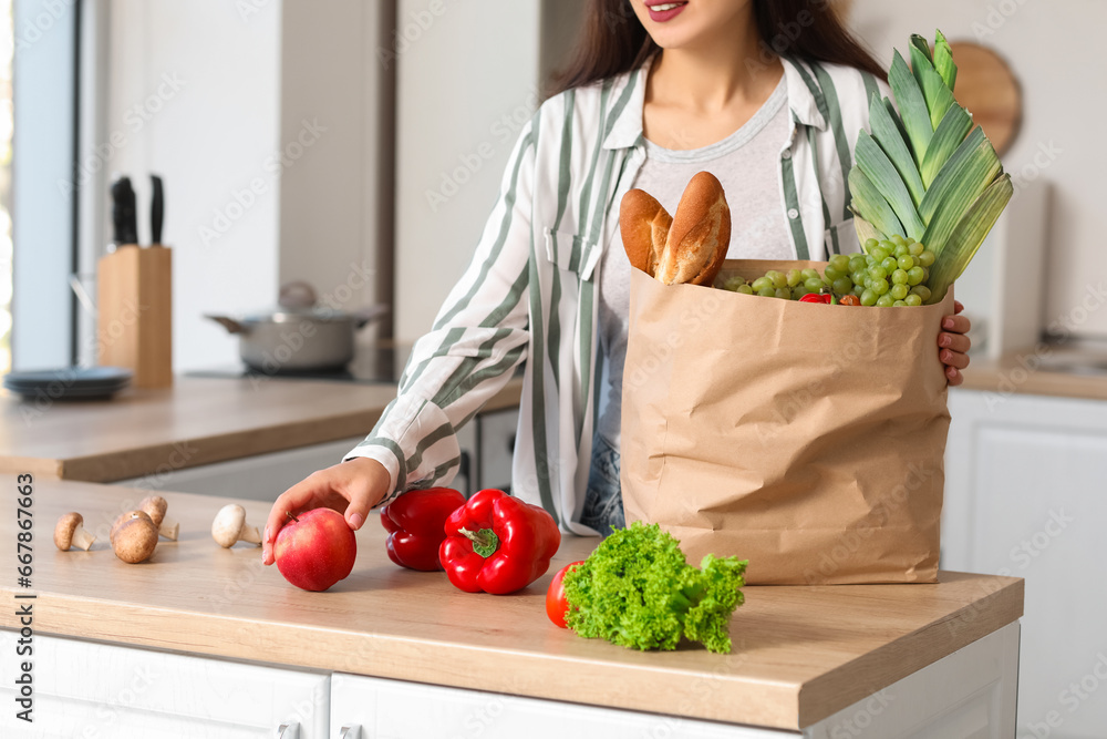 Young Asian woman unpacking fresh products from market at table in kitchen