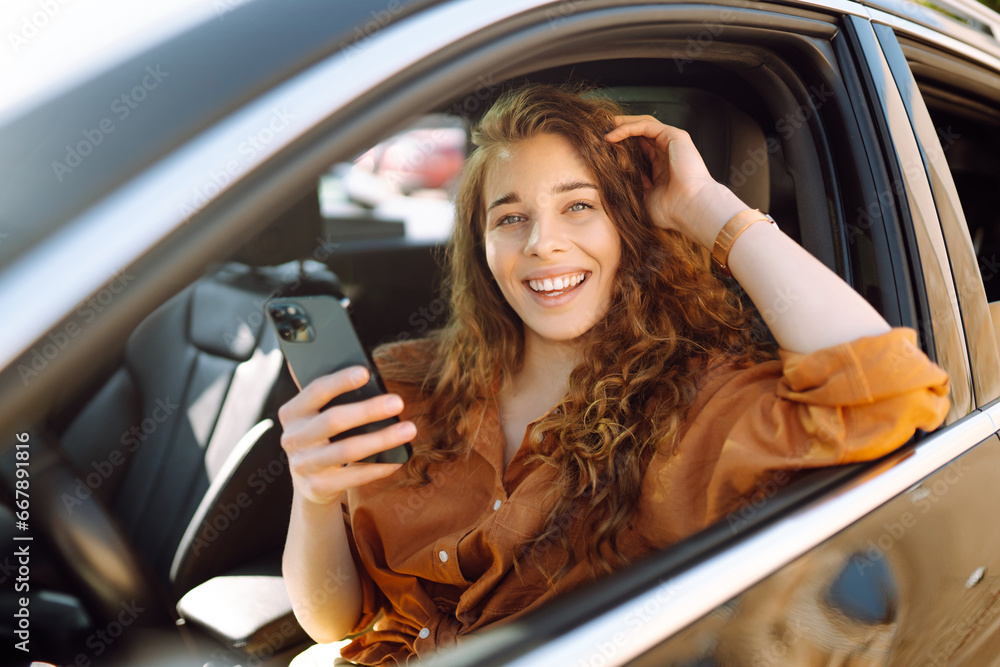 Beautiful woman driver in a car with a phone in her hands. The driver of the car uses a smartphone. Leisure, travel, technology, navigation.