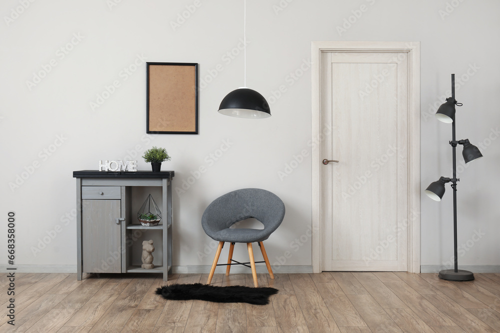 Interior of living room with stylish grey armchair and modern cabinet near white wall