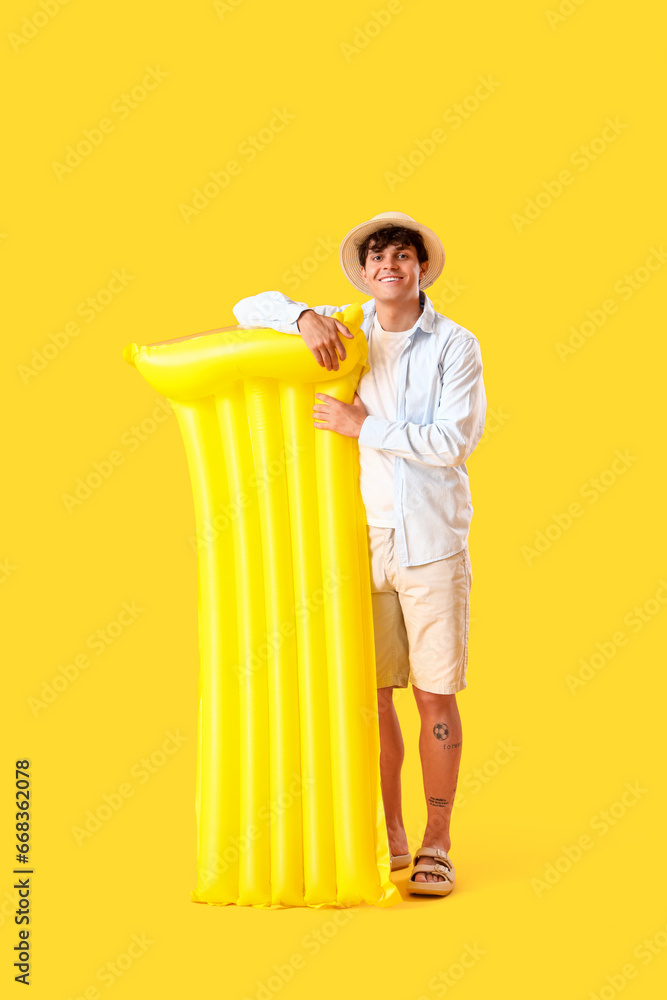 Young man with swim mattress on yellow background