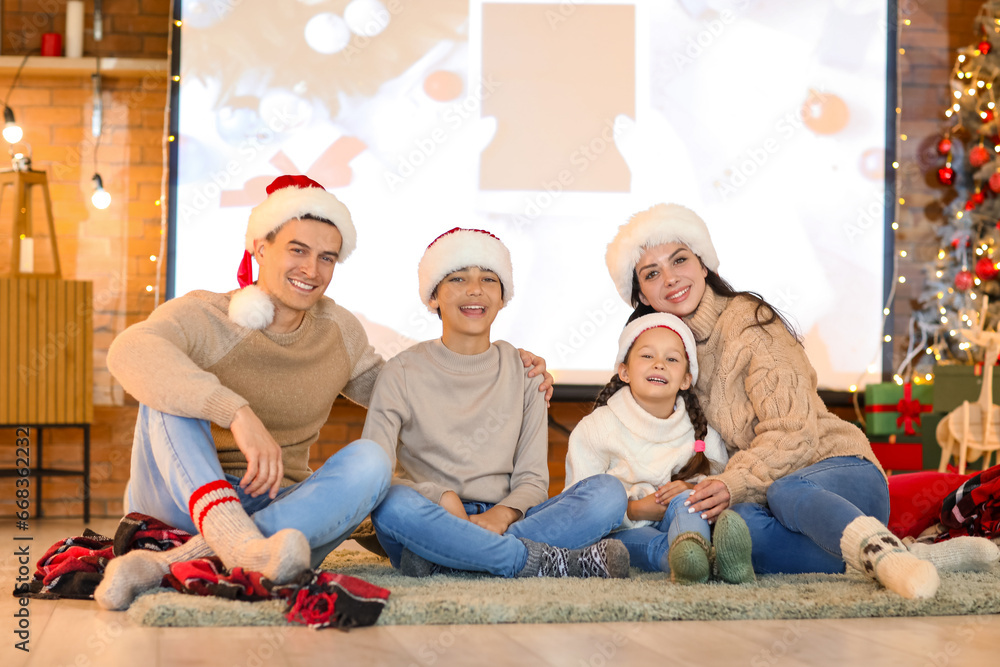 Happy family in Santa hats watching Christmas movie on projector screen at home