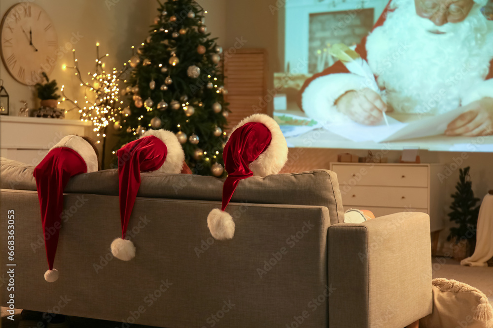 Young women in Santa hats watching Christmas movie on projector screen at home, back view