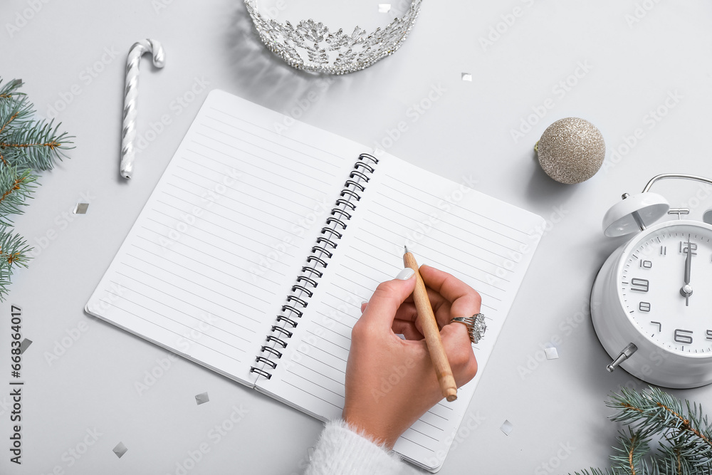 Woman writing in notebook with Christmas decor and tiara on light background, closeup