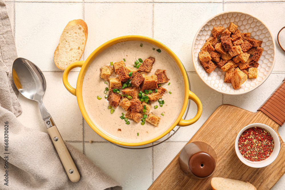 Pot of tasty cream soup with croutons on white tile background