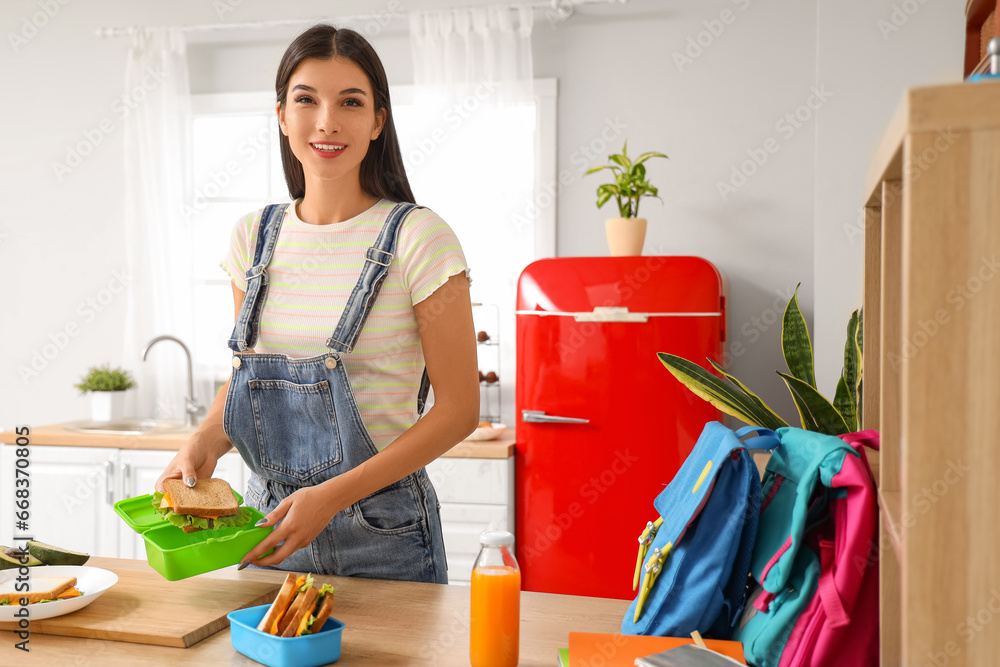 Young woman putting sandwich in school lunchbox at home