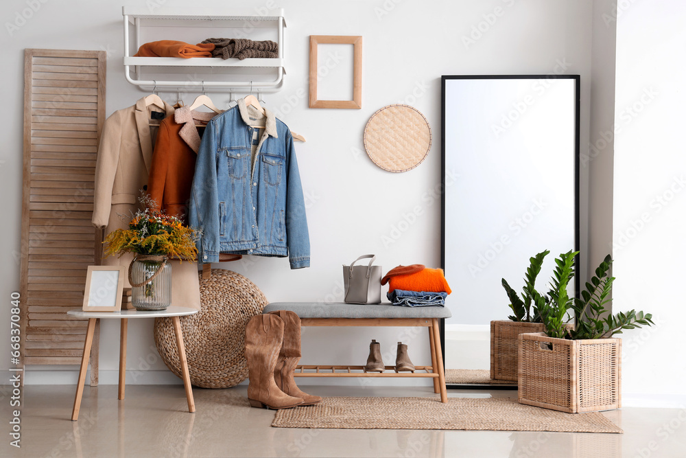 Interior of modern hallway with autumn clothes, mirror and bench