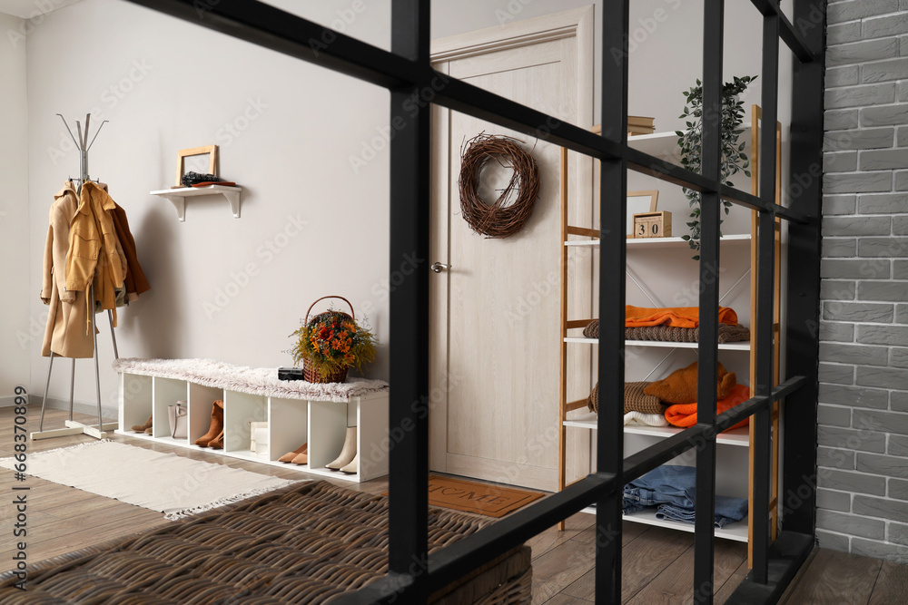 Interior of modern hallway with stylish clothes, shoes and autumn decorations, view through folding screen