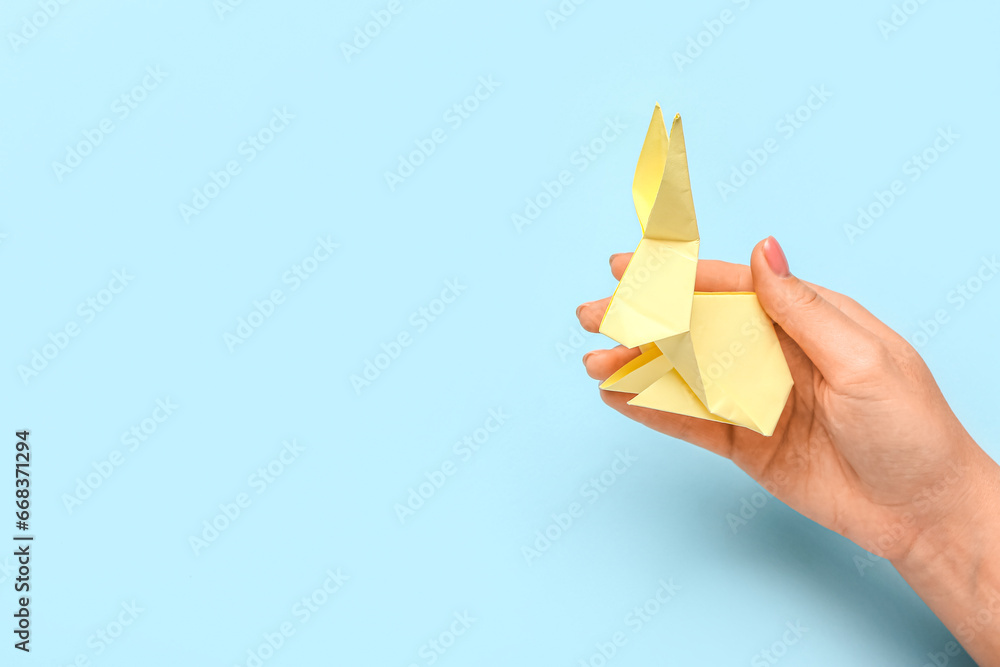 Female hand with beige rabbit on blue background