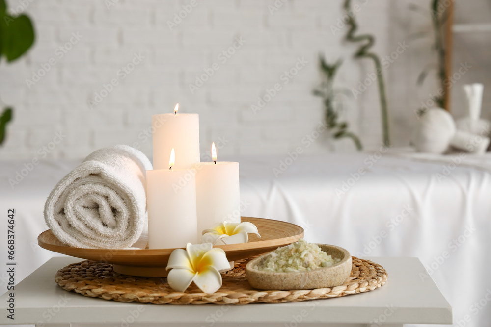 Spa composition with burning candles and flowers on table in salon, closeup