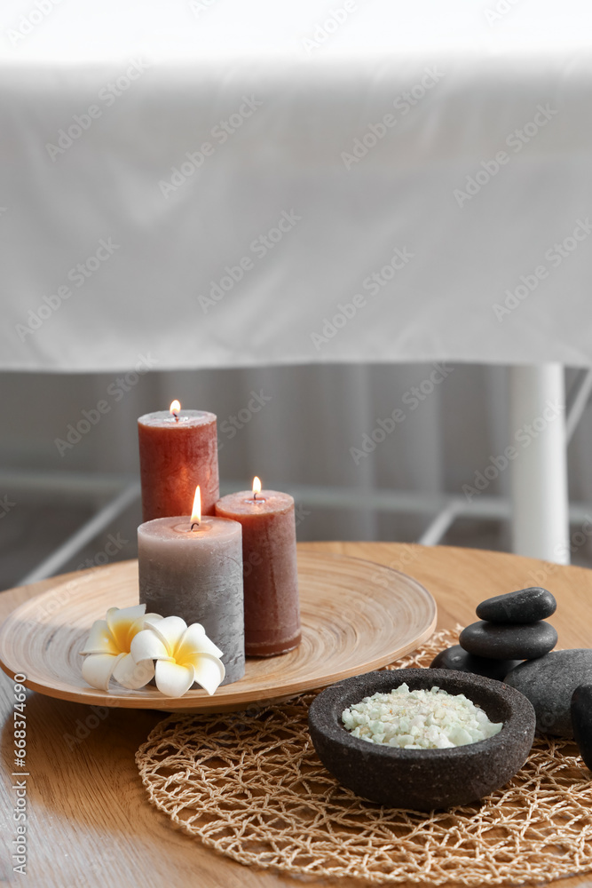 Burning candles with flower on table in spa salon, closeup