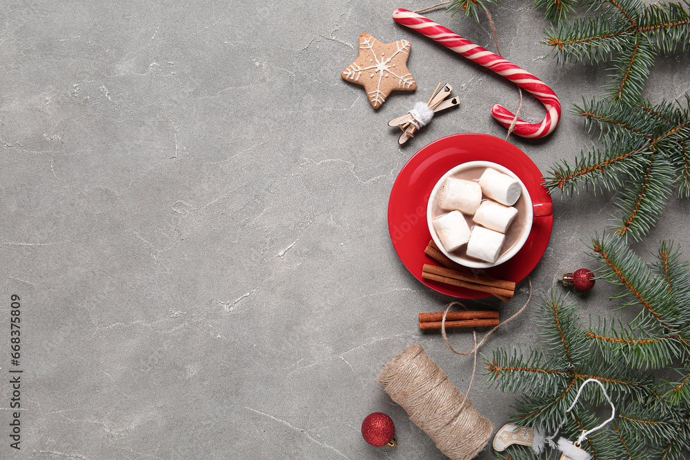 Cup of tasty Christmas cocoa with marshmallows, candy cane, fir branches, cinnamon, balls, cookie and rope on grey background