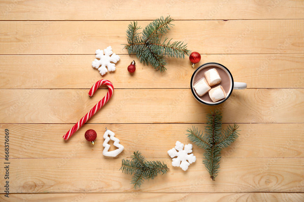 Frame made of tasty Christmas cocoa with marshmallows, snowflakes, balls, candy cane and fir branches on wooden background