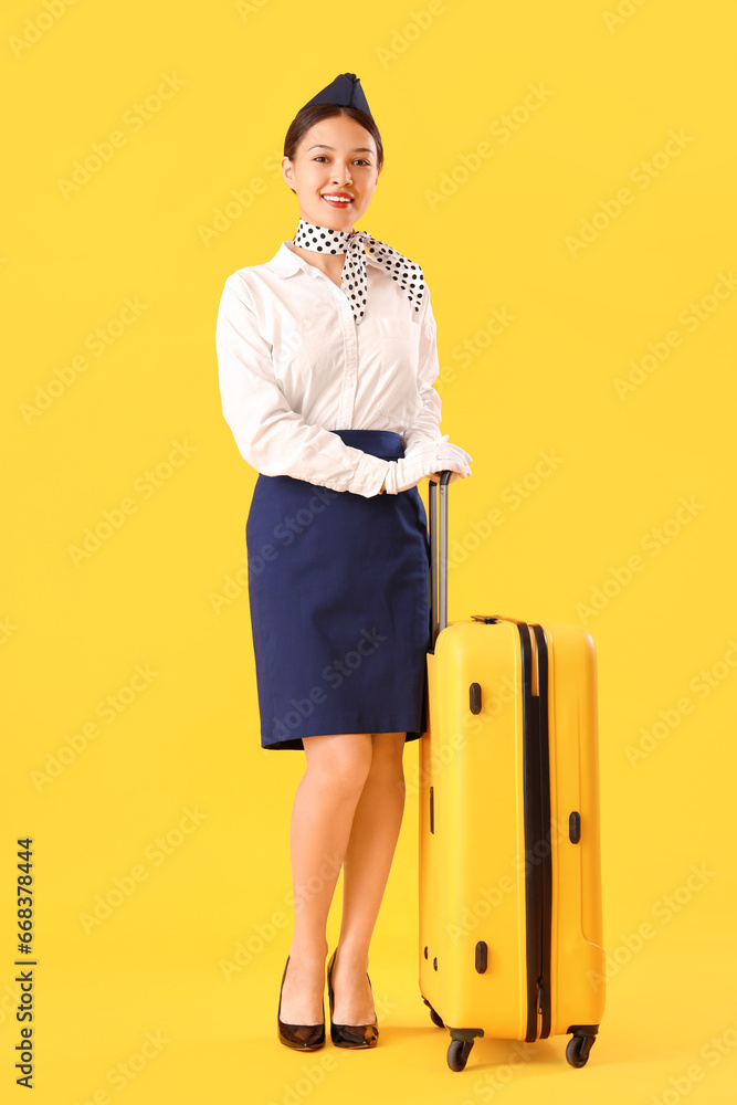 Beautiful Asian stewardess with suitcase on yellow background