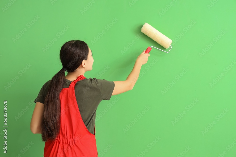 Female Asian decorator with paint roller on green background, back view