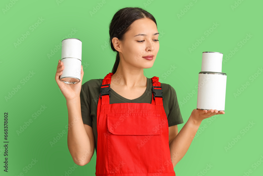 Female Asian decorator with paint cans on green background