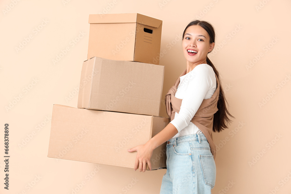 Young Asian woman with parcels on beige background