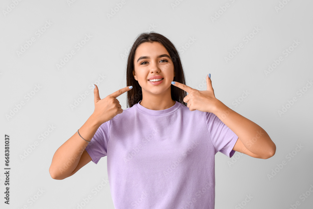 Young woman pointing at her smile on light background