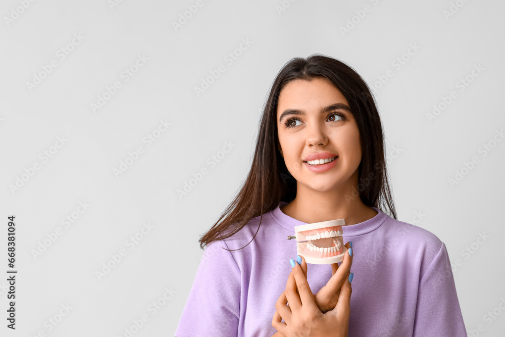 Smiling young woman with jaw model on light background