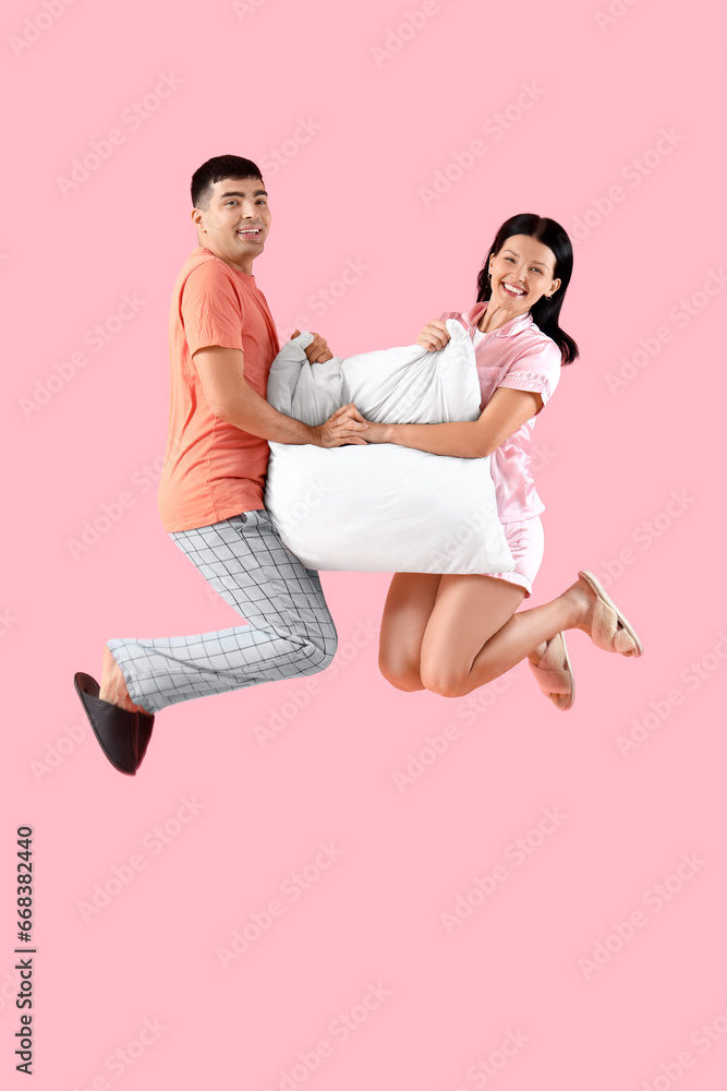 Young couple with pillow jumping on pink background