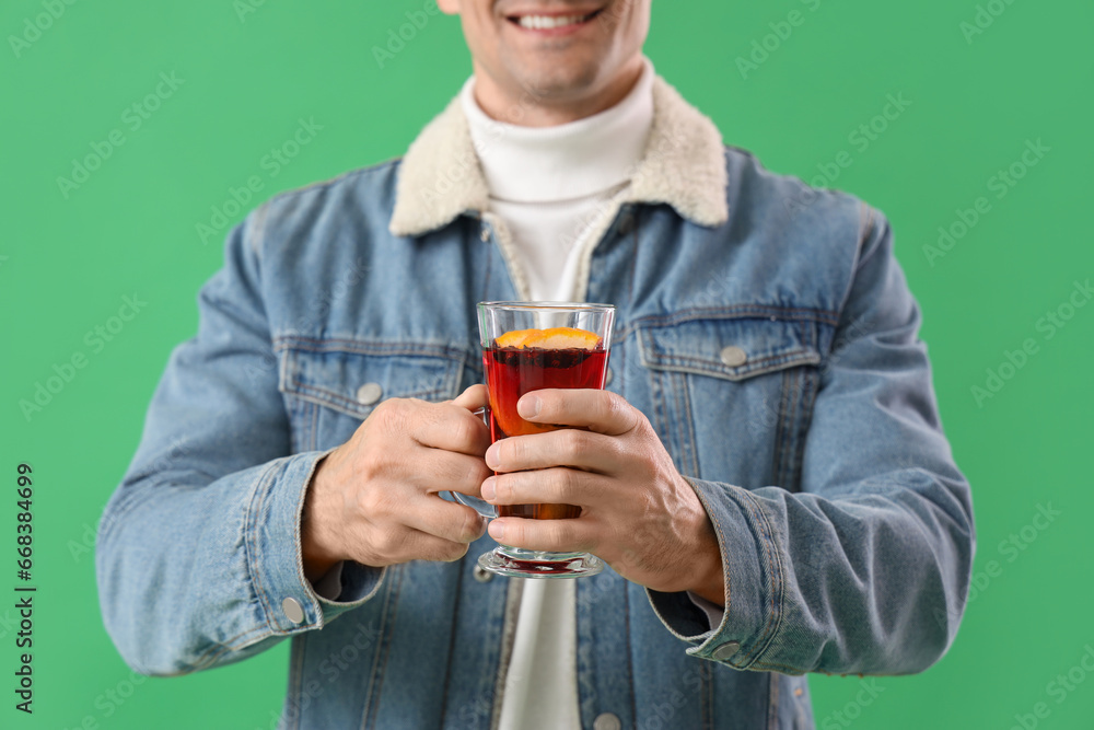 Handsome man with glass of mulled wine on green background, closeup