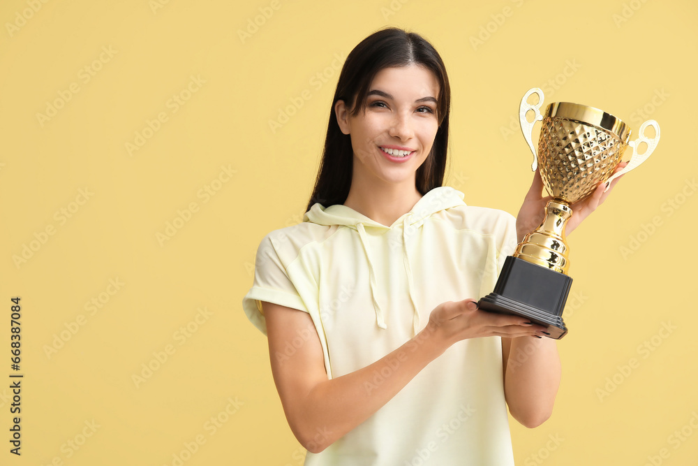 Sporty young woman with gold cup on yellow background