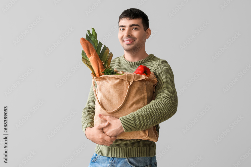 Young man with grocery bag on grey background