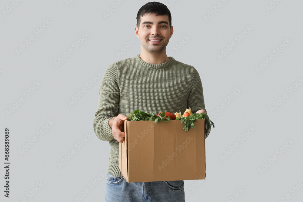 Young man with grocery box on grey background