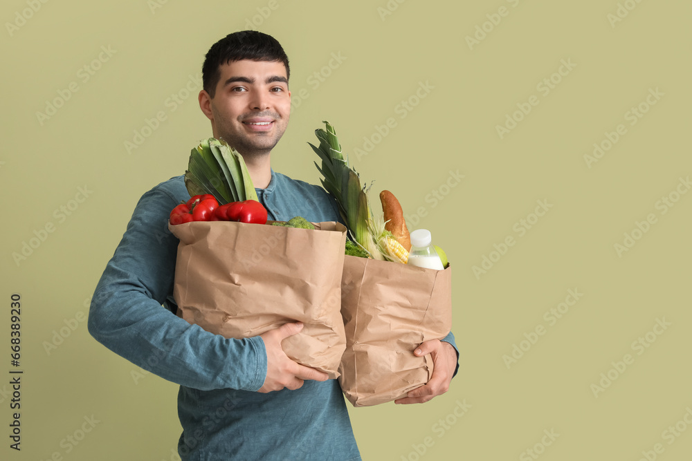 Young man with grocery bags on green background