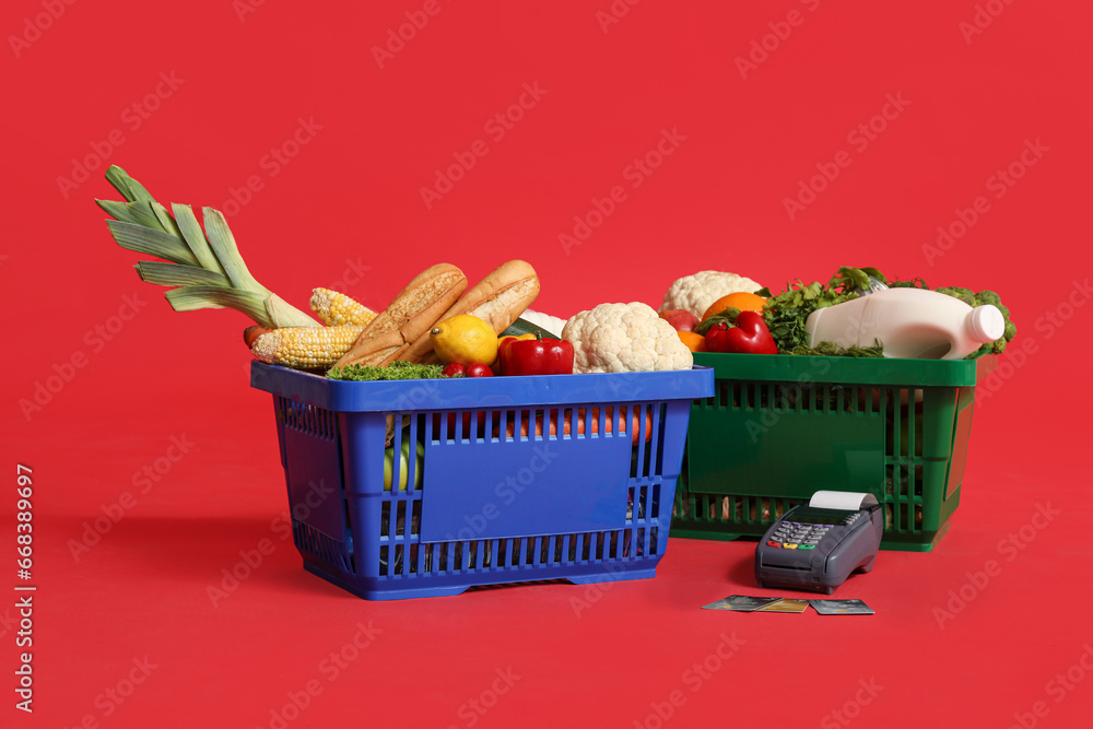 Shopping baskets full of food with payment terminal and credit cards on red background